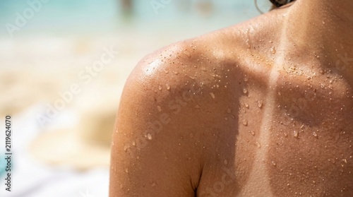 Close up of a tanned woman shoulder with water drops and sand grains on her skin, sunbathing on the beach in summer, vacation and skincare concept, healthy glow and body care photography.