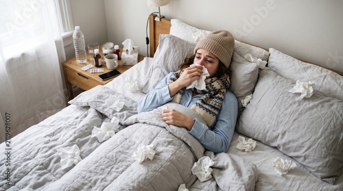 Sick woman wearing a winter hat and scarf feeling ill in bed with flu sickness infection healthcare influenza