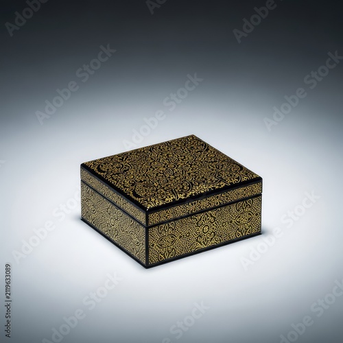 An elegant black jewelry box with intricate gold patterns sits perfectly centered on a smooth, minimalist gray studio background, isolated, luxury, sleek