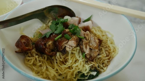 Dry Egg Noodles with Roasted Duck and Crispy Pork Belly Topped with Fresh Herbs, Served with Clear Soup on Marble Table