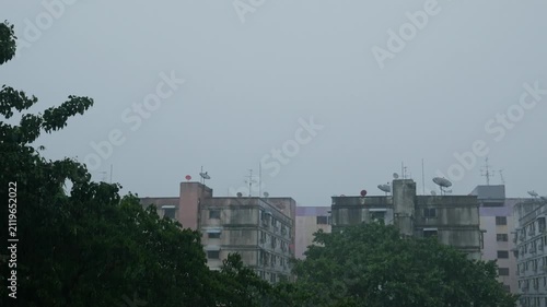 Stormy Monsoon Rain Over Old Residential Apartment Buildings with Satellite Dishes and Green Trees, Dark Gloomy Urban Cityscape
