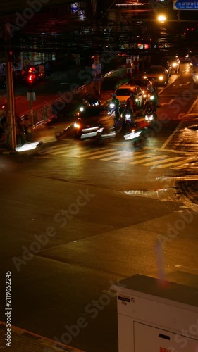 Editorial July 06 2026 — Time Lapse Night Traffic Light Trails at Busy Bangkok Intersection with Motorcycles Cars and Taxi, Wet Road Reflection Urban Street Scene Thailand