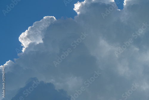 Towering cumulus cloud rising into bright blue sky with sunlit silver edge, soft billowing texture, strong contrast, and serene open atmosphere, with cumulus, cloud, sky, blue detail