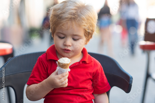 A baby enjoys ice cream on a summer day. Baby licks a sweet ice cream cone. Ice cream brings a smile to the babys face. A baby holds icecream. Baby tastes cold ice cream. Kid happiness.