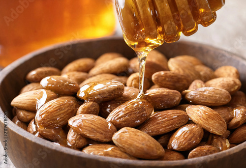 Golden honey drips onto toasted almonds in a rustic bowl