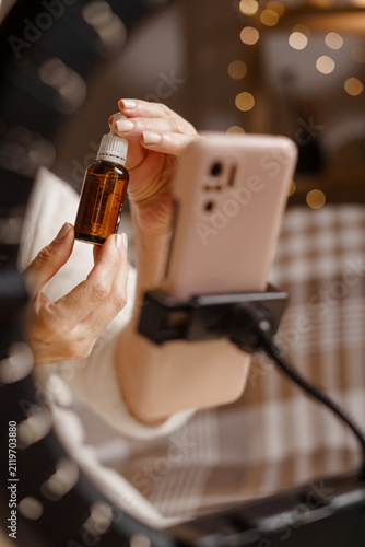 Beauty blogger promoting facial serum during live streaming with smartphone and ring light. Skincare, beauty influencer, cosmetic review and healthy skin
