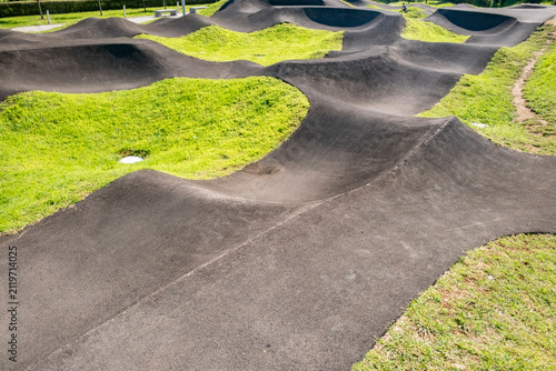 Bike riders practice on a pump track surrounded by grass on a sunny day in a local park
