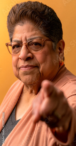 An assertive elderly woman pointing her finger directly at the viewer with a stern expression, conveying authority and a demand for attention