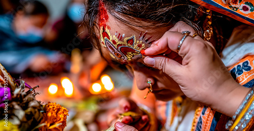 An Indian bride receives blessings and ornate decoration during a traditional wedding ceremony, illuminated by the warm glow of oil lamps