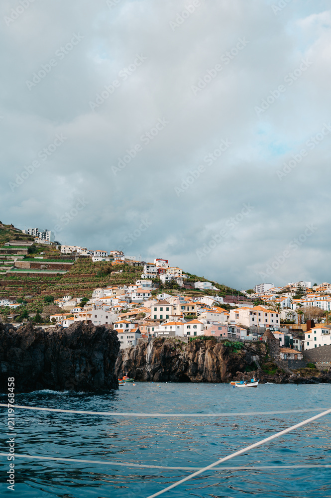 Obraz premium View of a coastal cliffside town from the water, Câmara de Lobos