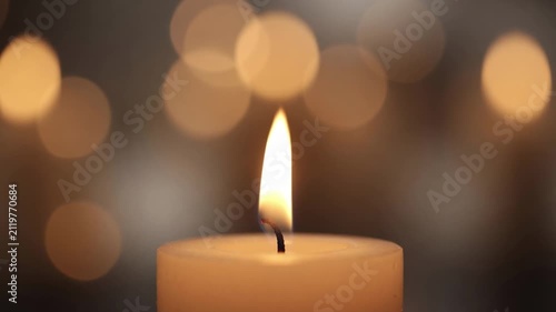 Single burning white candle with glowing warm bokeh background representing peace, hope, and memory