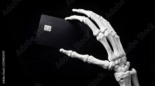 Skeleton hand holding blank black credit card on dark background with skeleton