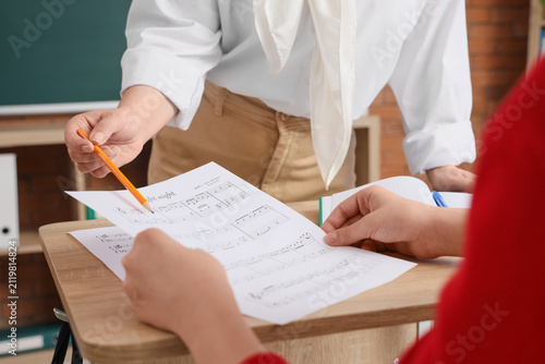 Teenage boy with teacher learning music notes in classroom, closeup