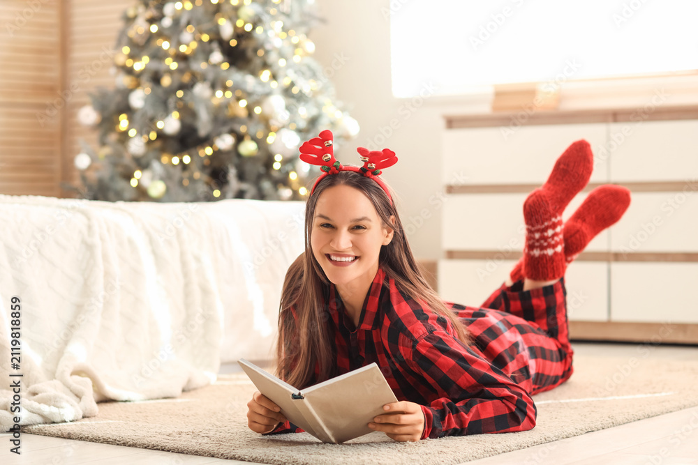 Fototapeta premium Young woman reading book in bedroom on Christmas eve