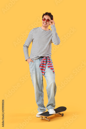 Happy young man in sunglasses with skateboard on yellow background