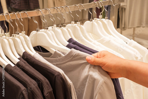 Man chooses white and black sweaters hanging on hanger in store.