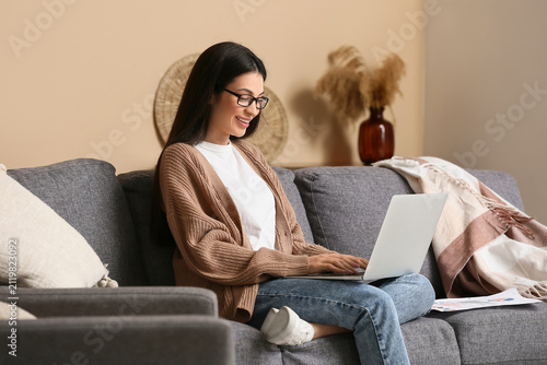 Beautiful young woman working with laptop and sitting on sofa in living room