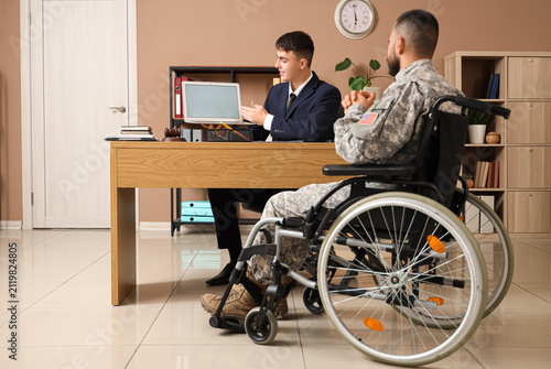 Male lawyer showing laptop to soldier in wheelchair at office