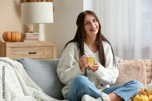 Beautiful young woman with cup of tea on autumn day at home