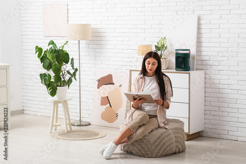 Konstfotografi Beautiful young woman reading book near portable table fan with humidifier in li