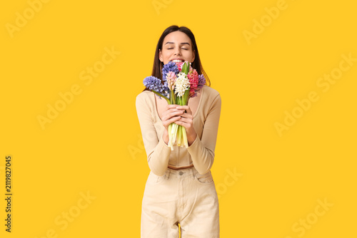Happy smiling young woman with hyacinth flowers on yellow background