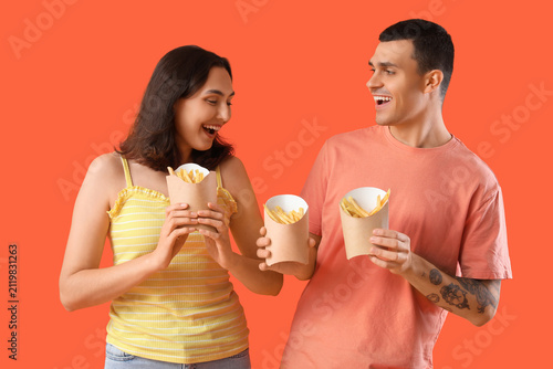 Beautiful young couple with french fries on orange background