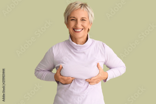 Fotografía Smiling mature woman checking her breast on green background
