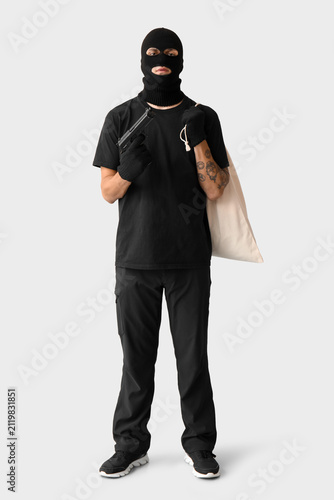 Male thief with gun and bag on grey background