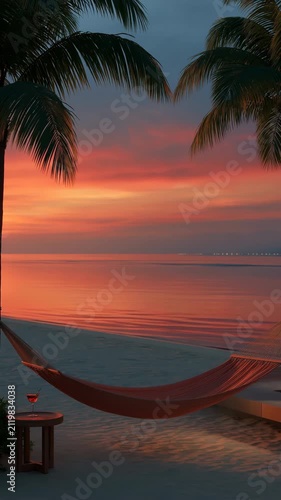 Hammock suspended between palms overlooking calm ocean sunset