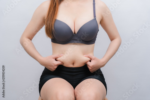Weight Management Awareness: A person in gym attire thoughtfully pinches the excess fat around their midsection, highlighting a focus on body health, personal fitness journey, and physical self-care.