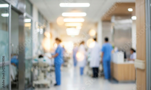 A blurred view of a hospital corridor with medical staff in blue scrubs attending to patients, showcasing a busy healthcare environment.