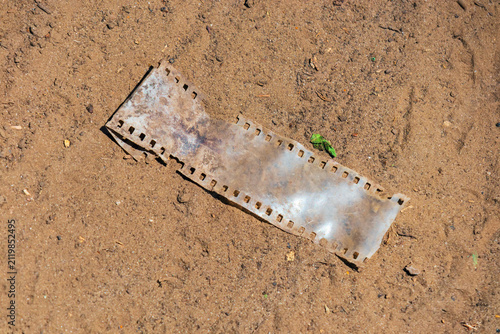 A piece of vintage 35mm photographic film lies abandoned on the ground in the sand. A close-up of the aged film on a dusty road