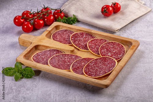 Fotografie Sliced salami in cheese on wooden board with tomatoes and basil