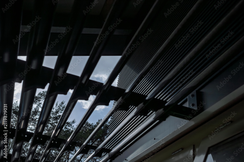 Fototapeta premium Abstract low-angle view of a black steel louvered canopy structure against a bright sky with clean modern lines.