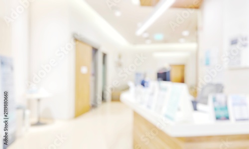 Blur abstract background of corridor in clean hospital. Blurry view of aisle in office with light floor. Defocus walkway in white light building hall with patient registration at reception desk.