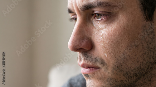 Sad man crying with tear rolling down cheek close up portrait copy space