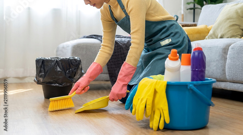 Woman sweeping dust and debris with broom and dustpan at home in celebration of national clean your floor day for household hygiene