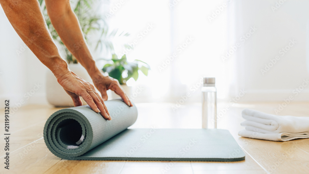 Fototapeta premium Yoga Mat Preparation: A person's hands are shown close-up as they neatly roll up a yoga mat on a wooden floor, ready for a session or put away after practice.