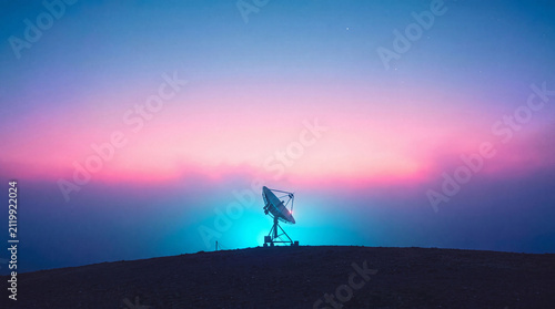 satellite dish antenna silhouette against a vibrant purple and blue sunset sky