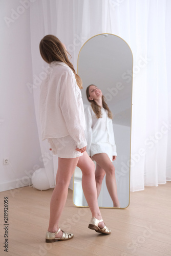Model standing near mirror in casual white outfit smiling positively