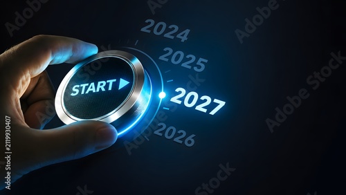 Person hand turning a glowing start button to select the year 2027 on a digital futuristic dashboard interface to represent the beginning of a new future and business goals for the year