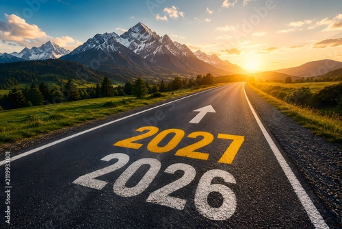 Numbers 2026 and 2027 painted on an asphalt road leading towards a beautiful mountain landscape at sunset representing the transition into a new year and future goals and progress