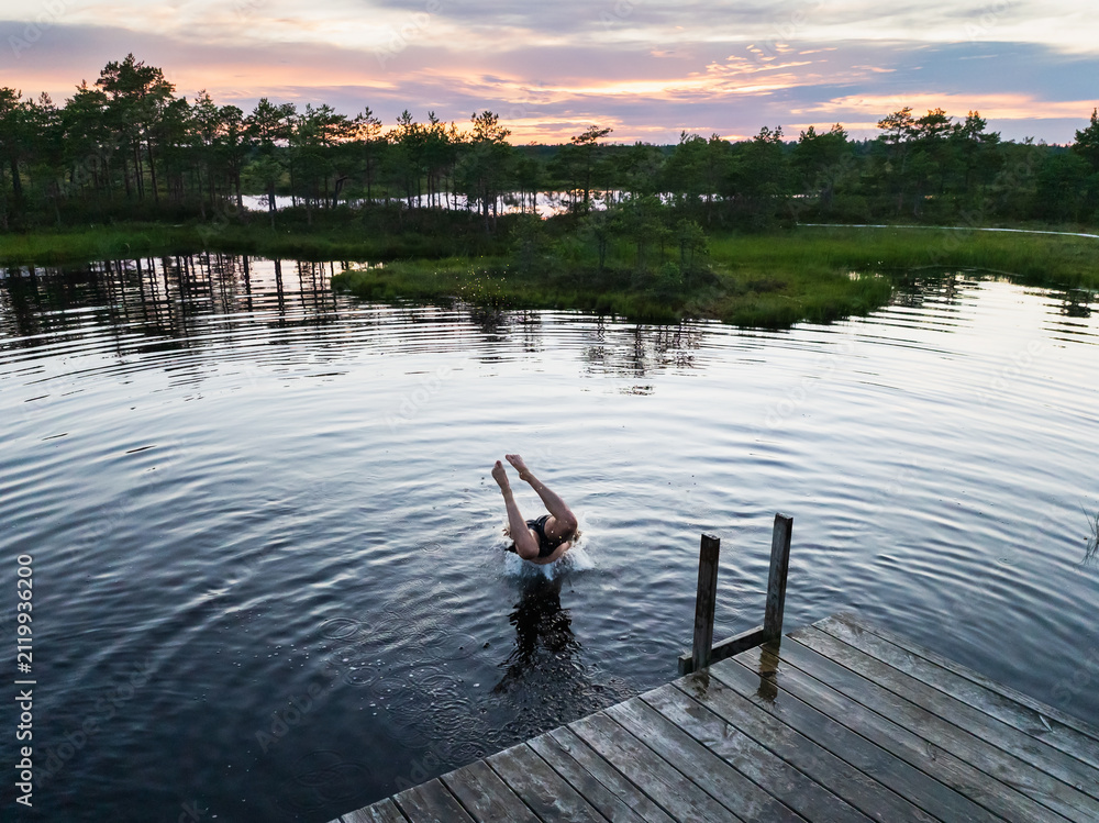 Fototapeta premium Man diving headfirst into bog lake from wooden pier during sunset in Estonian nature reserve outdoor summer swimming active lifestyle travel background