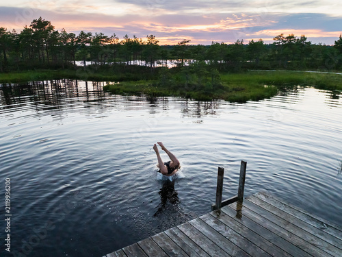 Man diving headfirst into bog lake from wooden pier during sunset in Estonian nature reserve outdoor summer swimming active lifestyle travel background