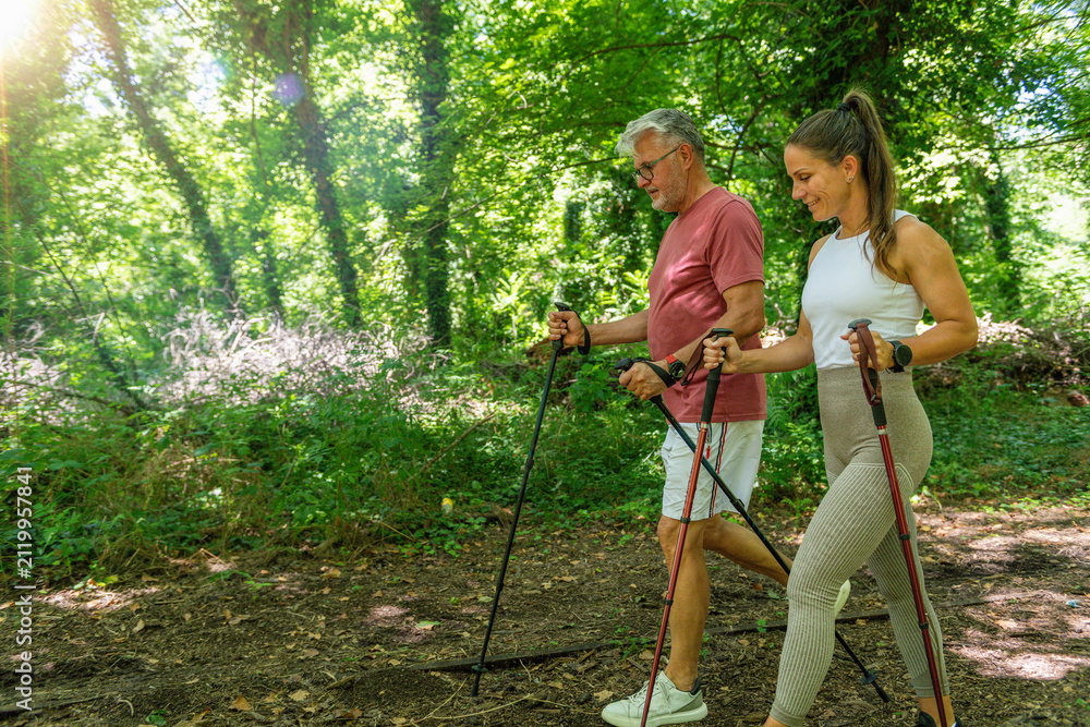 Fototapeta premium Senior participant performing a guided walking exercise using Nordic poles while receiving professional coaching to enhance cardiovascular fitness, functional movement, and healthy aging.