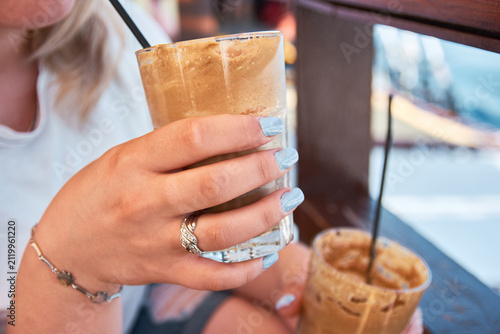 Close-up of a woman holding a tall glass of iced frothy coffee with a straw