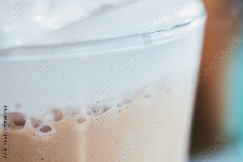 Close-up of a glass filled with frothy coffee beverage topped with creamy foam layer