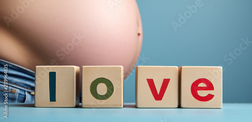Pregnant person shows belly with love blocks in front on blue background