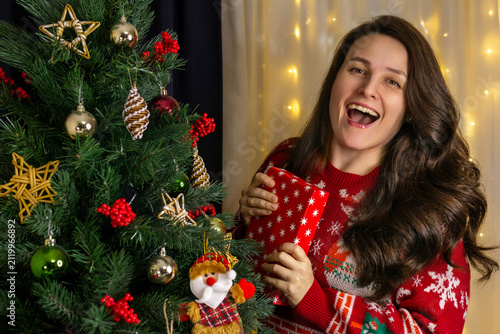 happy woman with a gift in her hands next to a Christmas tree