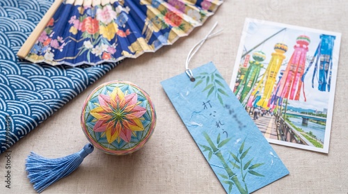 Traditional Japanese items including a colorful temari ball, a floral folding fan, a blue patterned fabric, a paper tag with bamboo, and a souvenir postcard